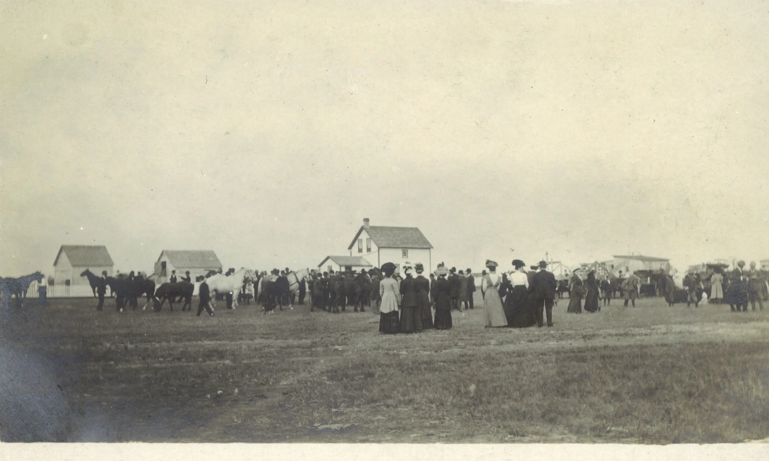 Crowd and horses gathered on a field near homes