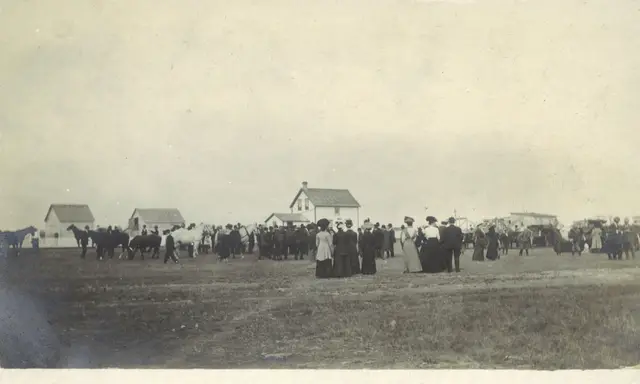 Crowd and horses gathered on a field near homes